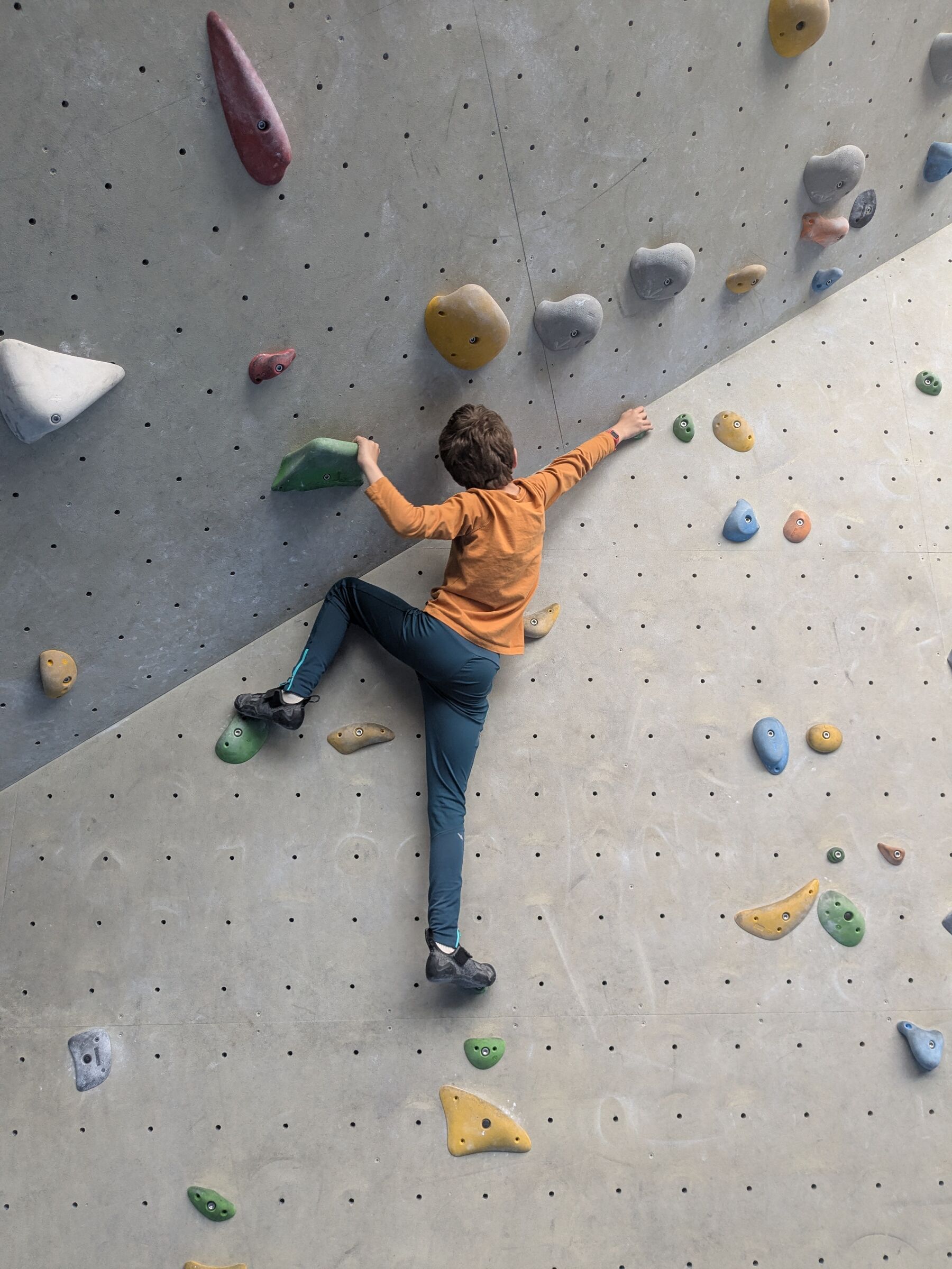 Oscar klimt tegen een muur met gekleurde klimgrepen